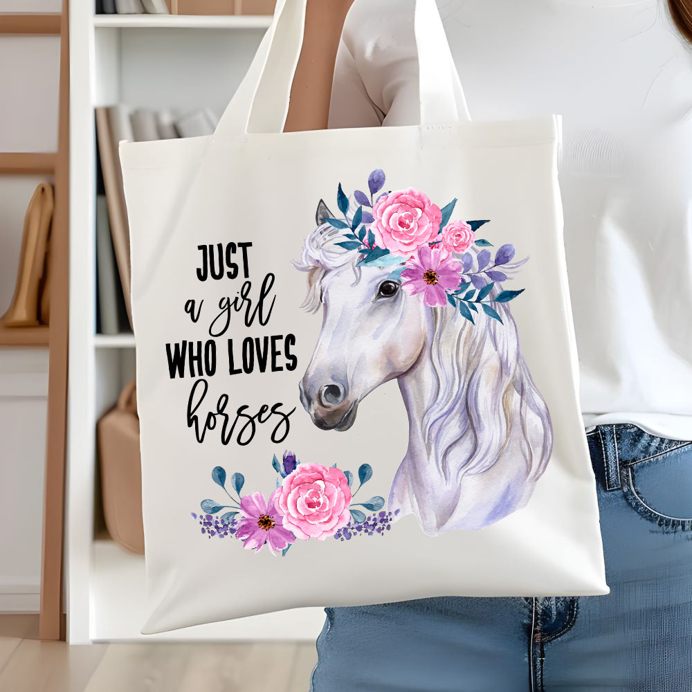 White long handled tote bag showing a white horse head shot and pink flowers decorating its mane. A quote decorates. A woman is holding the bag  in front of white book case.