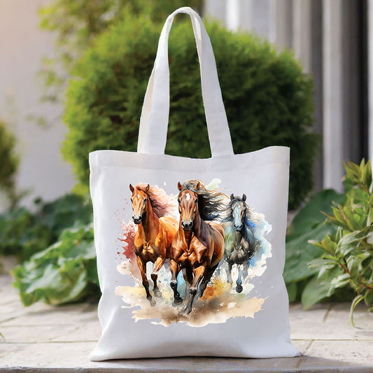 White tote bag with a long handle showing a trio of horses running through water. The bag is placed in front of a large green shrub with green foliage to the right side.