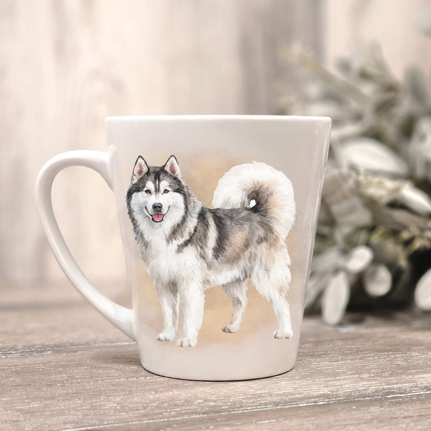 A Husky is standing on a white ceramic latte mug in a smoky background and looking forward.  The mug is placed on a wooden surface with sage green foliage to the right-hand side.