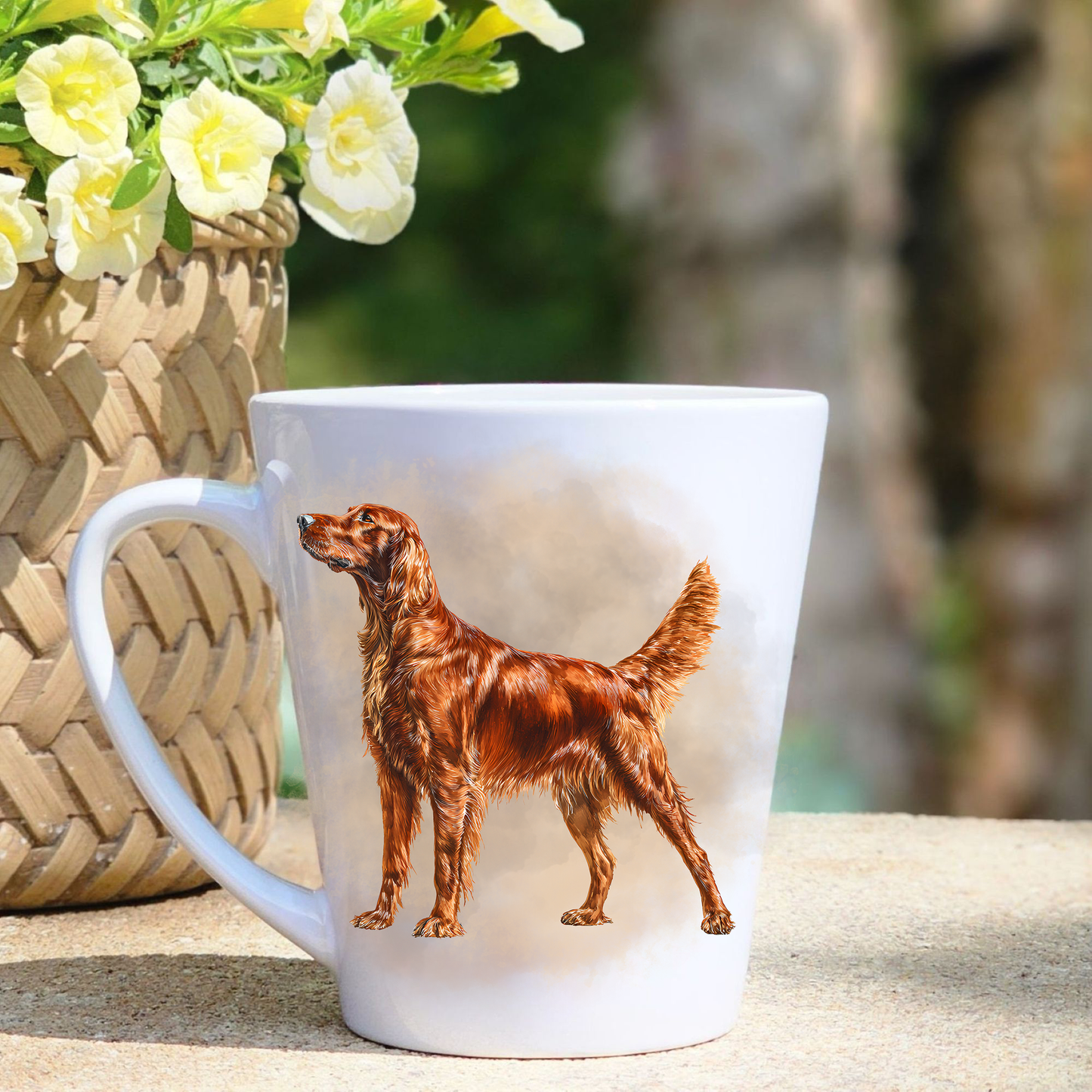 A white ceramic latte mug featuring a standing Irish Setter in a pink mist background.  A basket containing yellow flowers sits to the left-hand side.