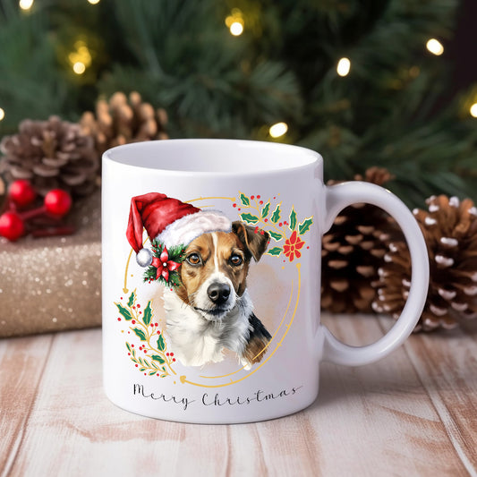 A white ceramic mug with a watercolor design of a Jack Russell Terrier wearing a Santa hat, surrounded by holly and berries, with the text 'Merry Christmas' on the bottom.