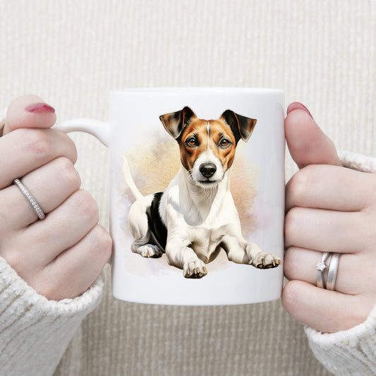 A woman is holding white ceramic mug showing a Jack Russell Terrier laying in front of a brown and gold misty background and facing forward.