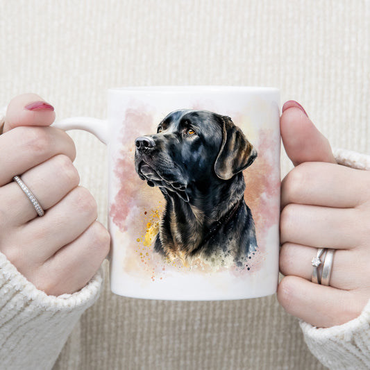 A watercolour image of a black Labrador dog looking to the left adorns this white ceramic mug. A pink and gold misty background decorates the mug which is being held by a woman with both hands.