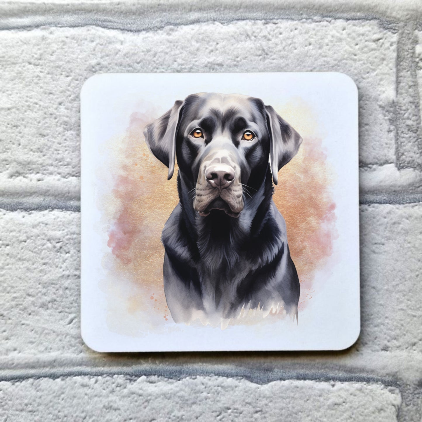 A White drinks coaster with a head shot of a Black Labrador with a pink and gold misty background.  The coaster is placed on a grey, brick effect surface.