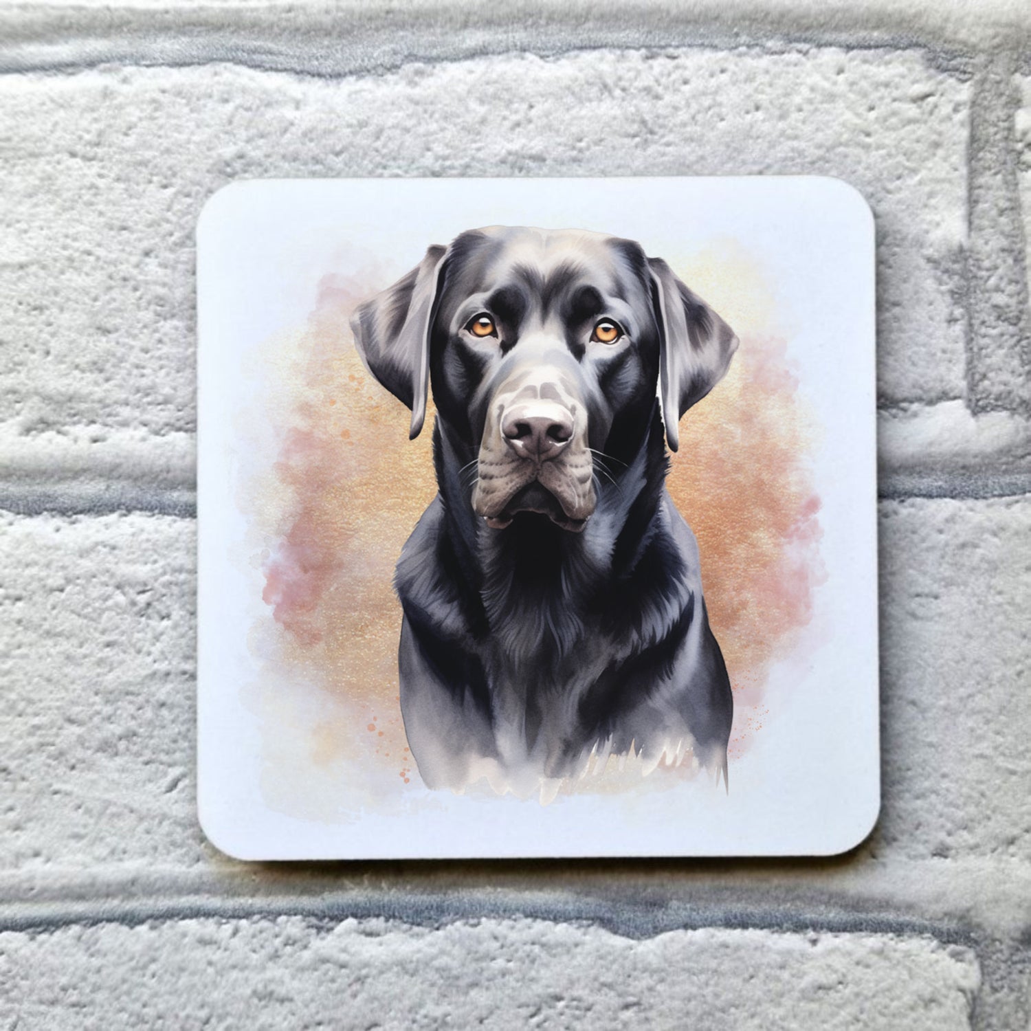 A White drinks coaster with a head shot of a Black Labrador with a pink and gold misty background.  The coaster is placed on a grey, brick effect surface.