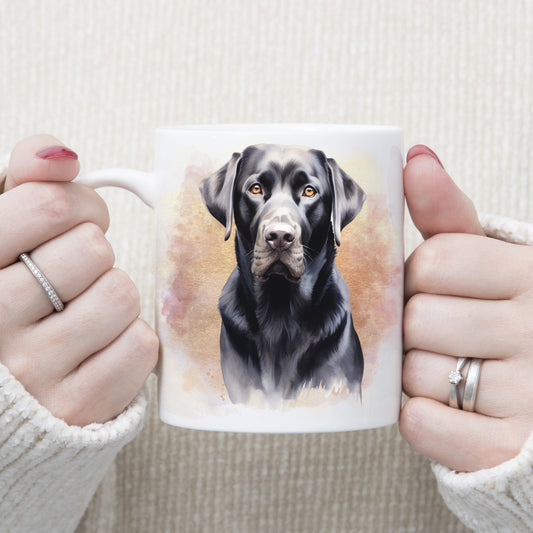 A head shot of a black Labrador dog sitting in front of a pink and gold misty background on a white ceramic mug. A woman is holding the mug