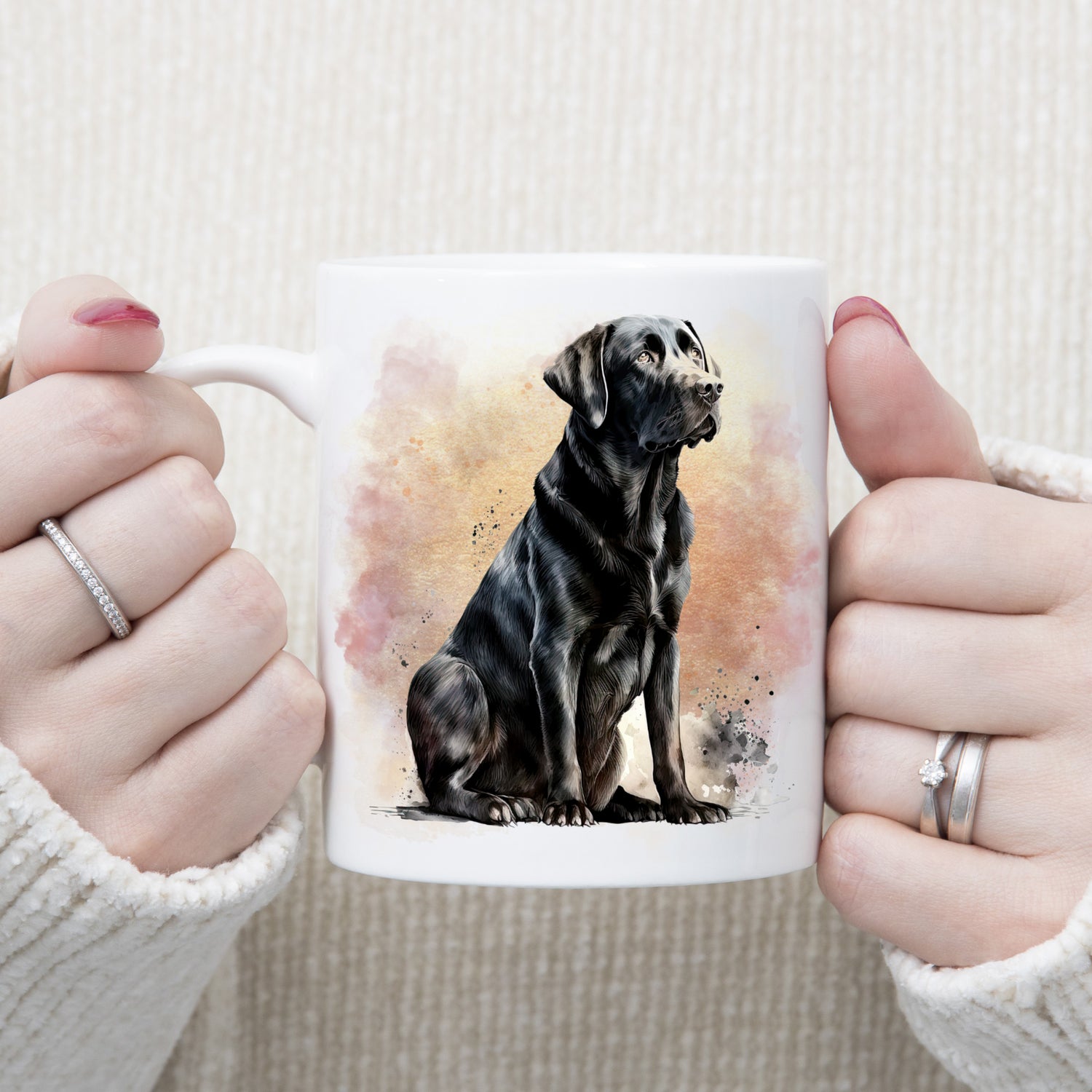 Image of a Black Labrador dog sitting with a pink and gold smoky background. The mug is being held by a  woman wearing rings.