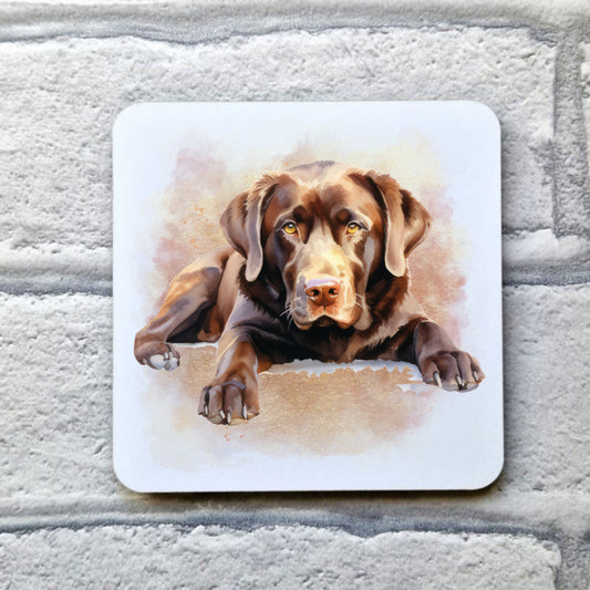 A Chocolate Labrador with amber eyes is laid facing forward among a pink and gold misty background on a white coaster. The coaster is placed on a grey, brick effect surface.