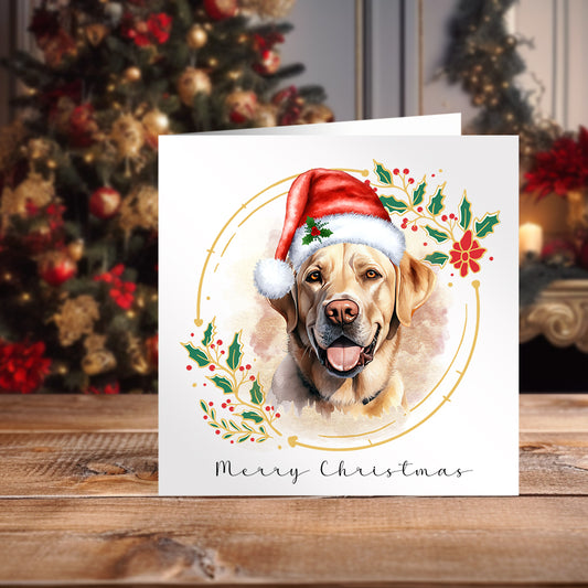 Labrador facing forward and wearing a Santa hat on a Christmas themed card. Positioned on a wooden surface with a decorated Christmas tree behind.