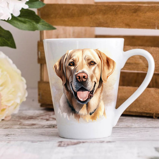 A latte coffee mug with a vibrant watercolor design of a yellow Labrador Retriever dog, placed on a wooden surface with flowers and a book in the background.