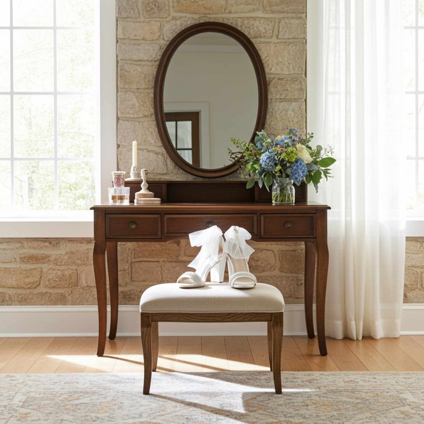 Wooden vanity with mirror, open-toe bridal shoes on a stool, and flowers in a room with stone wall and window.