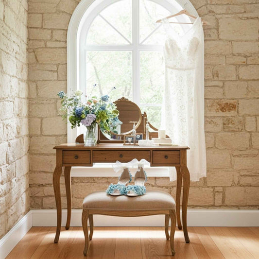 Wooden vanity table with mirror, flowers, and floral bridal shoes with peep toe on stool against a stone wall.