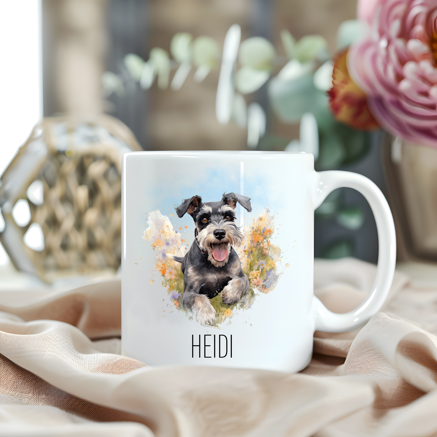 Image of a Miniature Schnauzer running through a field of flowers on a white personalised ceramic mug which has been placed on a beige cloth.  A large pink flower with green foliage accessorizes the image.