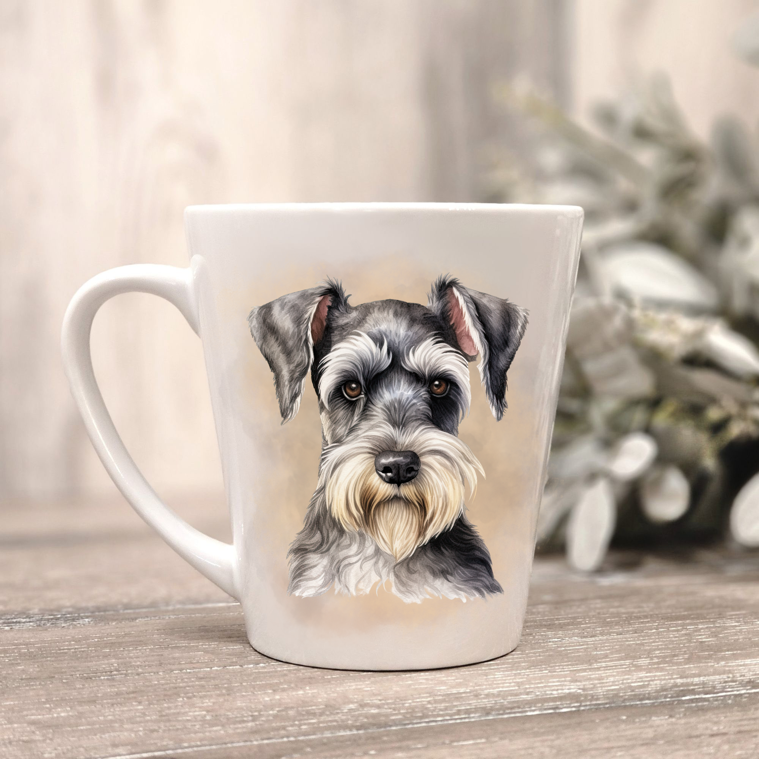 A Miniature Schnauzer is shown in a sitting position on a white ceramic latte mug in a smoky background and looking forward.  The mug is placed on a wooden surface with sage green foliage to the right-hand side.