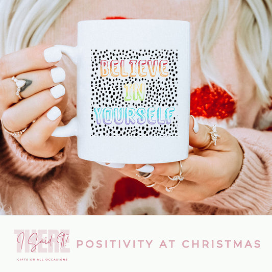 A person holding a white ceramic mug with a colourful text pattern that reads 'BELIEVE IN YOURSELF'