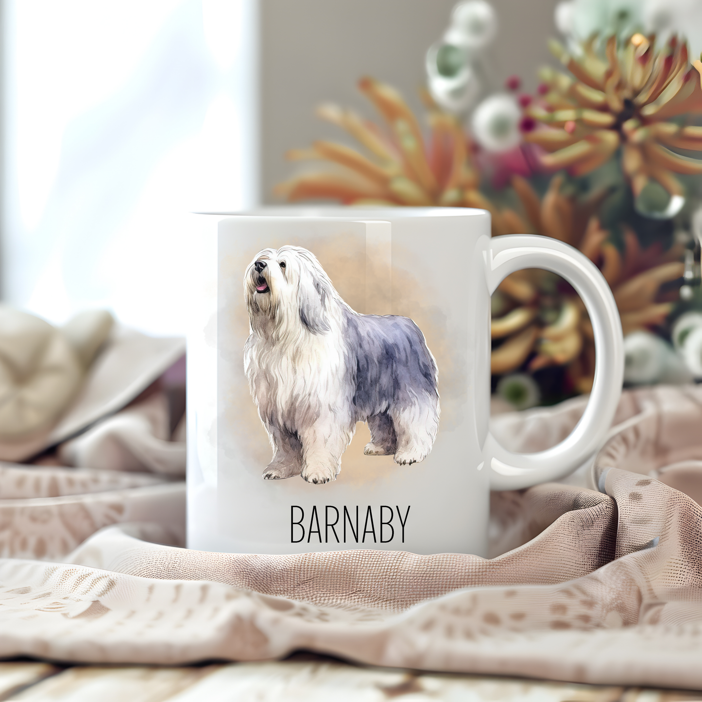 Personalised coffee mug featuring an Old English Sheepdog on a white ceramic mug which has been placed on a beige cloth.  Stems of large  flowers accessorizes the image.