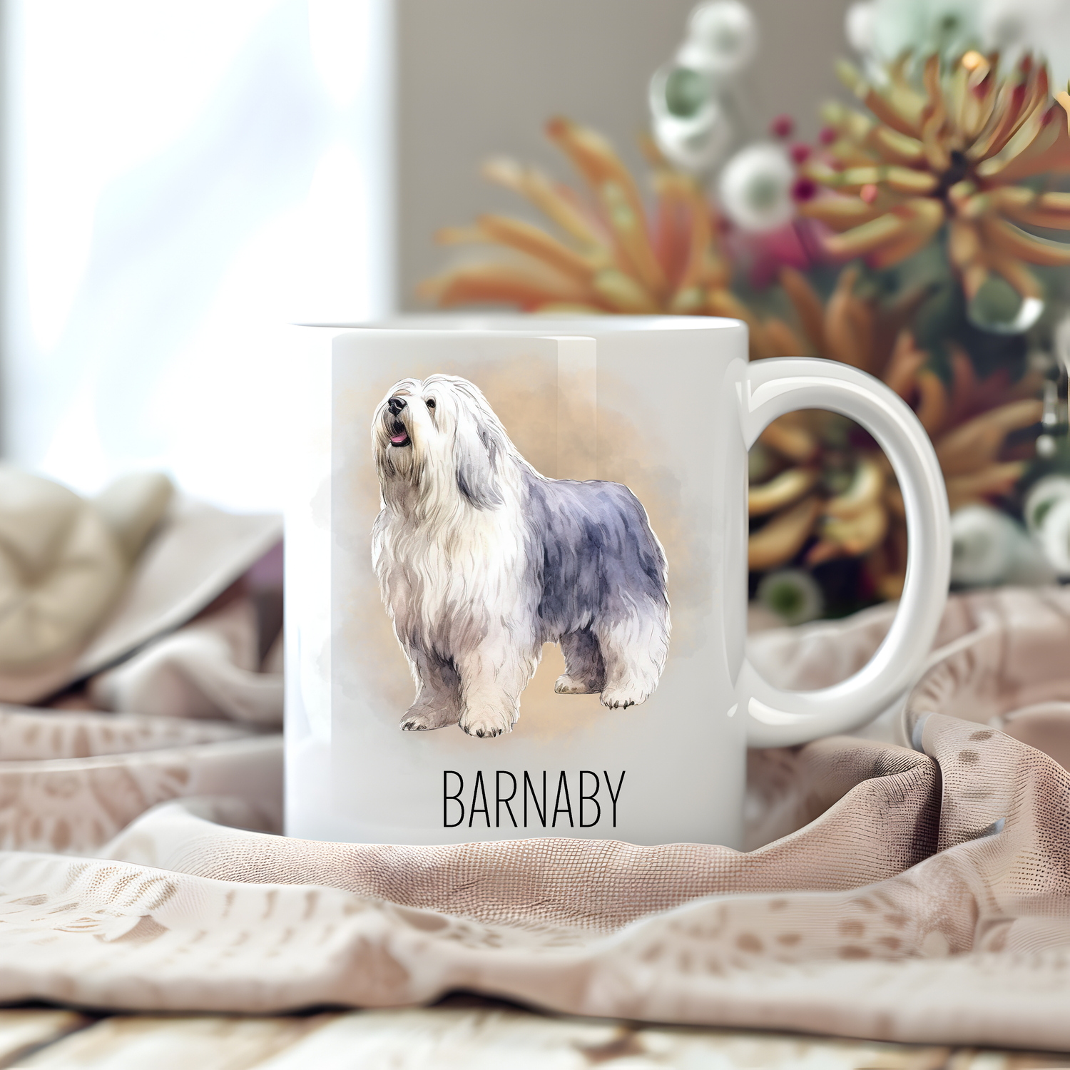 Personalised coffee mug featuring an Old English Sheepdog on a white ceramic mug which has been placed on a beige cloth.  Stems of large  flowers accessorizes the image.