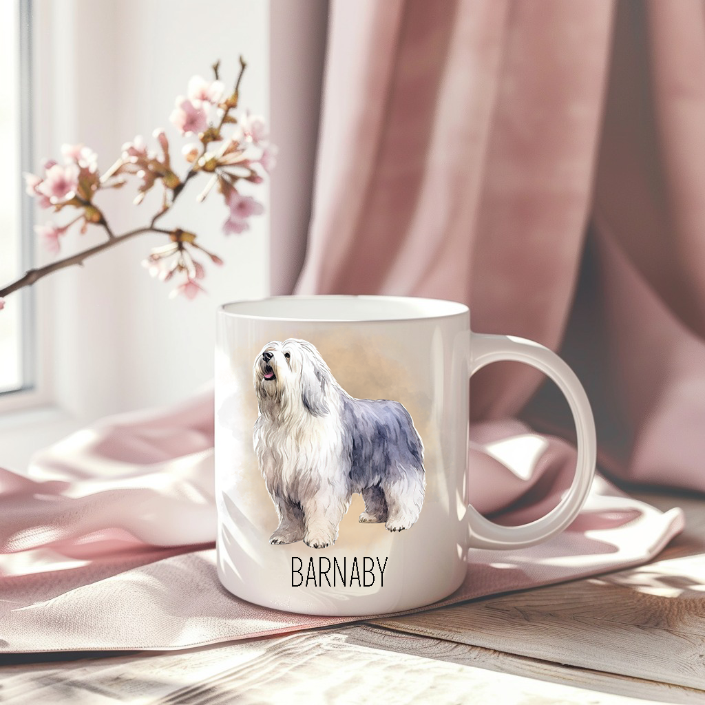 An Old English Sheepdog is standing on a personalised white ceramic mug which has been placed on a pink drape.   A stem of small pink flowers accessorizes the image.