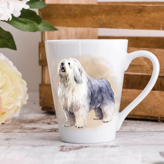 A white ceramic latte mug stands on a wooden surface with a crate in the background. The mug features an Old English Sheepdog. A large yellow flower peeps in from the left-hand side.