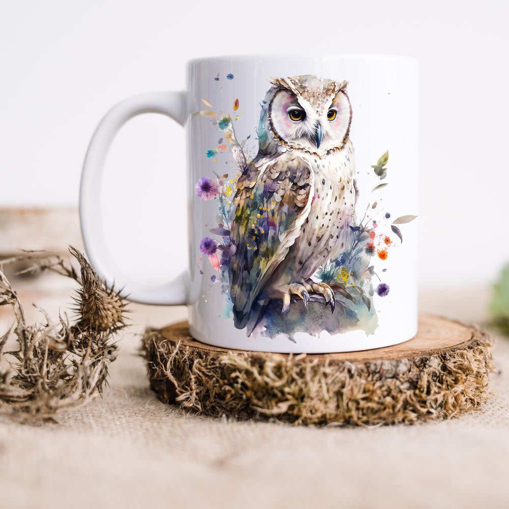 A Barn Owl sits perched among colourful wildflowers on a white ceramic mug.  The mug is placed on a thick wooden disc and a dried thistle is set to the left hand side.
