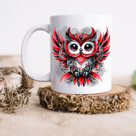 White ceramic mug showing a Gothic Owl with red and black feathers on a smoky grey background. The mug is placed on a rustic wooden disc. .