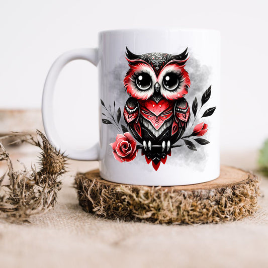 Ceramic mug in white showing a Gothic Owl with red and black feathers and perched on a rose stem. The image is finished with a smoky grey background. The mug is placed on a rustic wooden platform