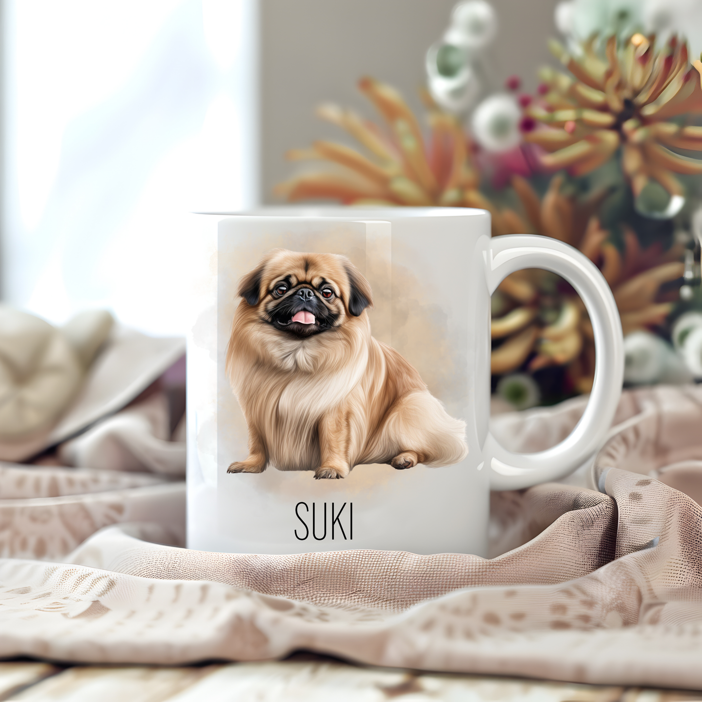 Personalised coffee mug featuring a seated Pekingese dog on a white ceramic mug which has been placed on a beige cloth.  Stems of large  flowers accessorizes the background.