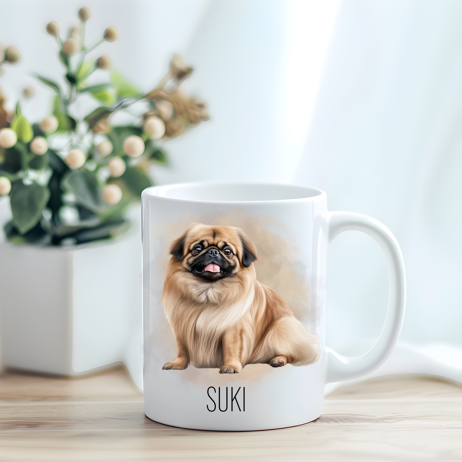 This coffee mug features a Pekingese on a white ceramic mug which has been placed on a light wooden surface.  A green and white plant sits on the left side of the image in a square plant pot.