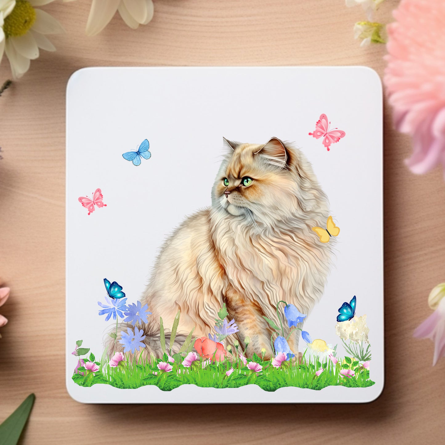 White coaster showing a Ginger Persian cat surrounded by flowers and butterflies while sat on grass. The coaster is placed on a wooden surface with floral decoration