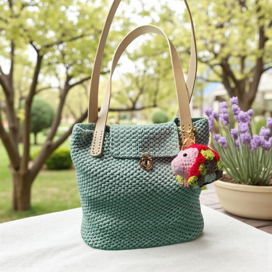 Green crochet handbag with a decorative crochet pig key ring  charm on a table outdoors
