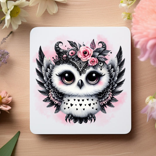 White coaster showing a cute Gothic Owl with black and pink feathers, and pink roses on a pink smoky background. The coaster is placed on a wooden surface with floral decoration.