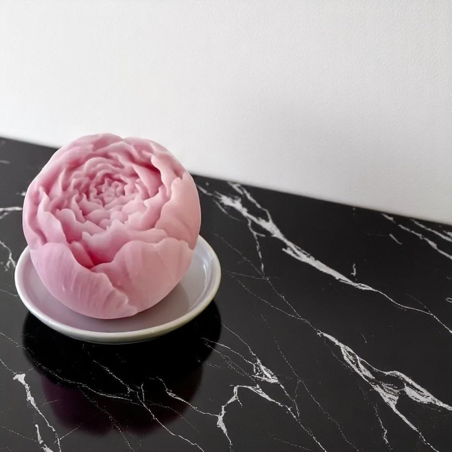 Pink flower-shaped wax melts on a white plate against a black marble background