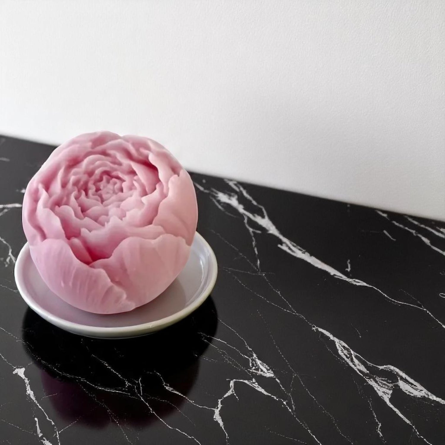Pink flower-shaped wax melts on a white plate against a black marble background