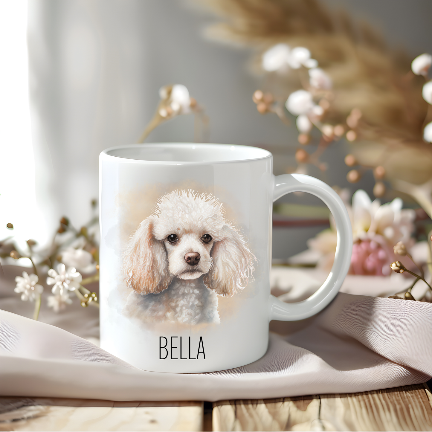 A lovely Poodle coffee mug personalised with a pet name.  The mug is sat on a wooden surface with a creamy coloured cloth and a variety of flowers decorate the background.