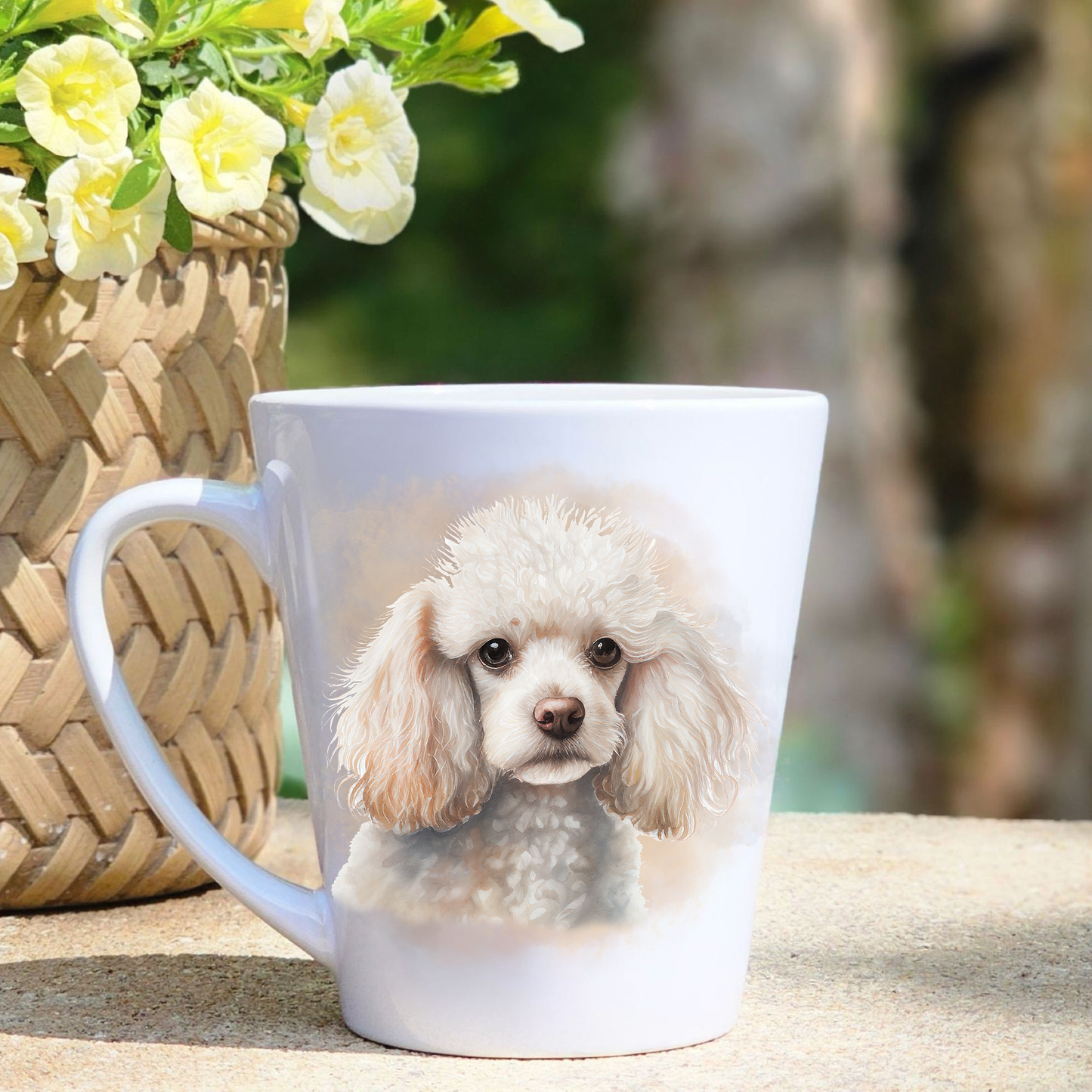 A white ceramic latte mug featuring a white Miniature Poodle in a gold/beige mist background.  A basket containing yellow flowers sits to the left-hand side. 
