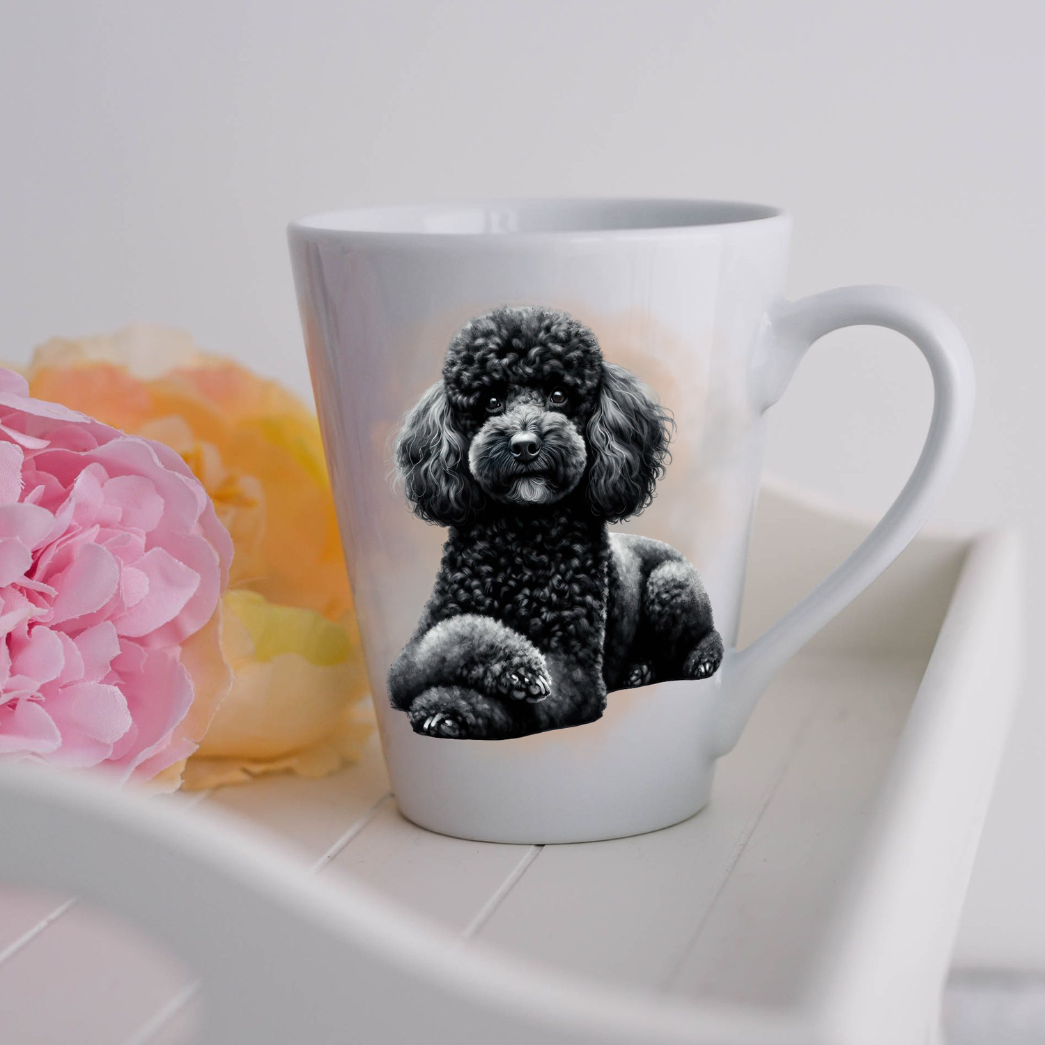 A black Miniature Poodle is shown lying on a white ceramic latte mug in a smoky background and looking forward.  The mug is placed on a white tray with pink and yellow flowers.