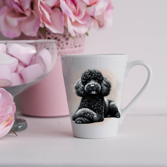 A Black Miniature Poodle is shown on a white ceramic latte mug in a smoky background and looking forward.  The mug is placed on a white surface with pink flowers in a pink plant pot and a dish of pink marshmallows.