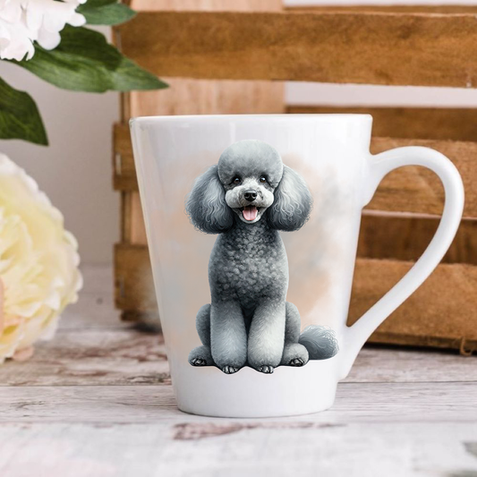 A white ceramic latte mug stands on a wooden surface with a wooden crate in the background. The mug features a smiling Grey Miniature Poodle.  A large yellow flower peeps in from the left-hand side.