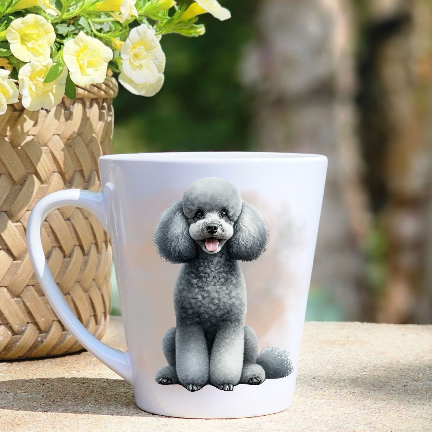 A white ceramic latte mug featuring a grey Miniature Poodle in a gold/beige mist background.  A basket containing yellow flowers sits to the left-hand side.