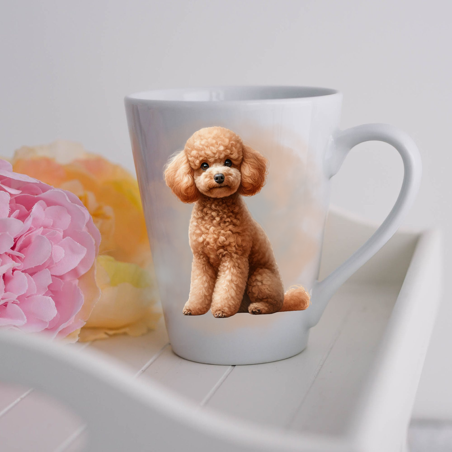 An Apricot Miniature Poodle is seen on a white ceramic latte mug in a smokey background and looking forward.  The mug is placed on a white tray with pink and yellow flowers.