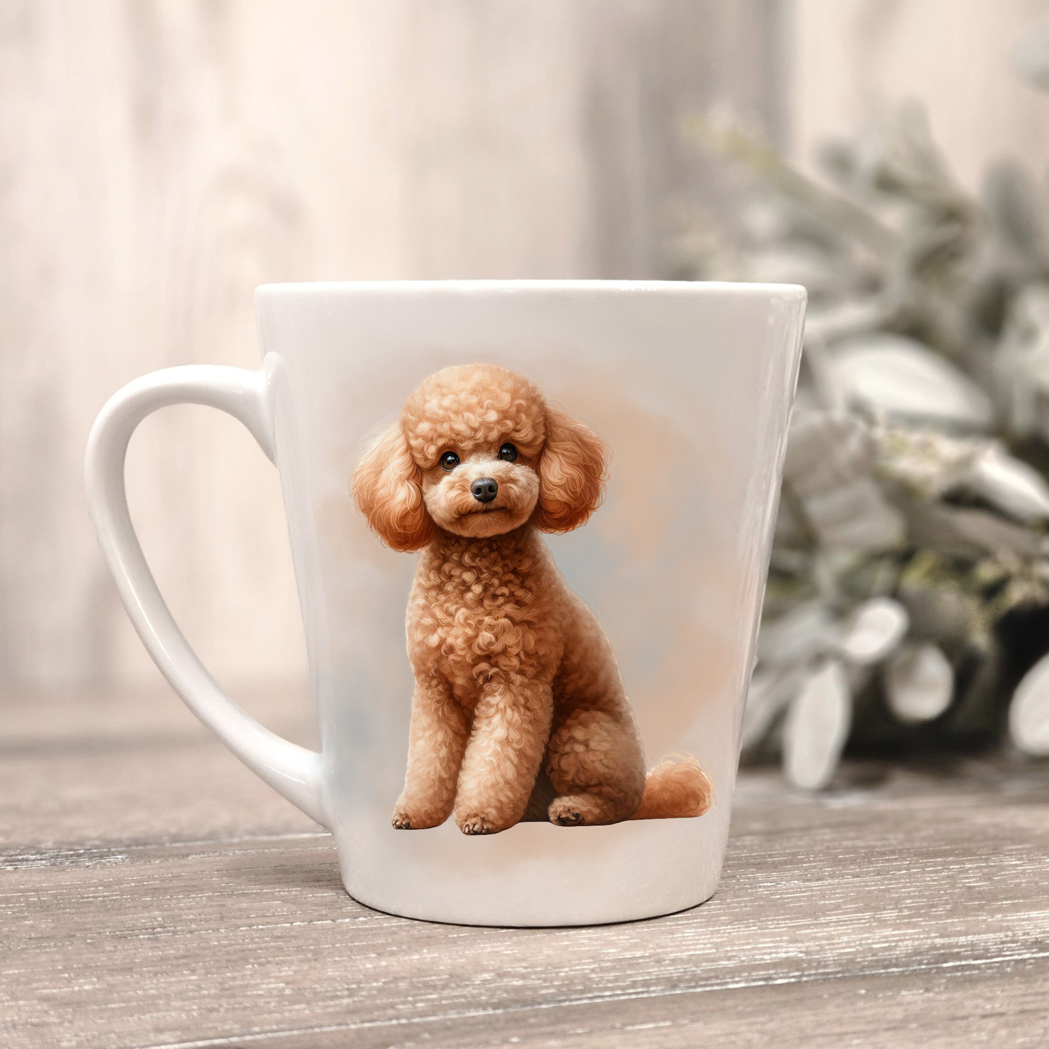 An Apricot Miniature Poodle is shown on a white ceramic latte mug in a smokey background and looking forward.  The mug is placed on a wooden surface with sage green foliage to the right-hand side.