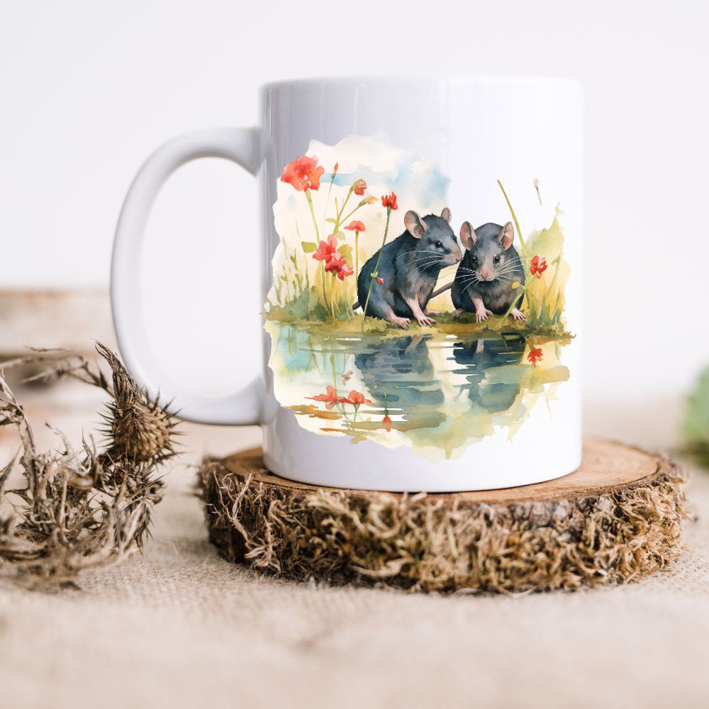 Two grey rats sat at the edge of water  with red flowers around and shown on a white ceramic mug.  The mug is placed on a rustic wooden disc.