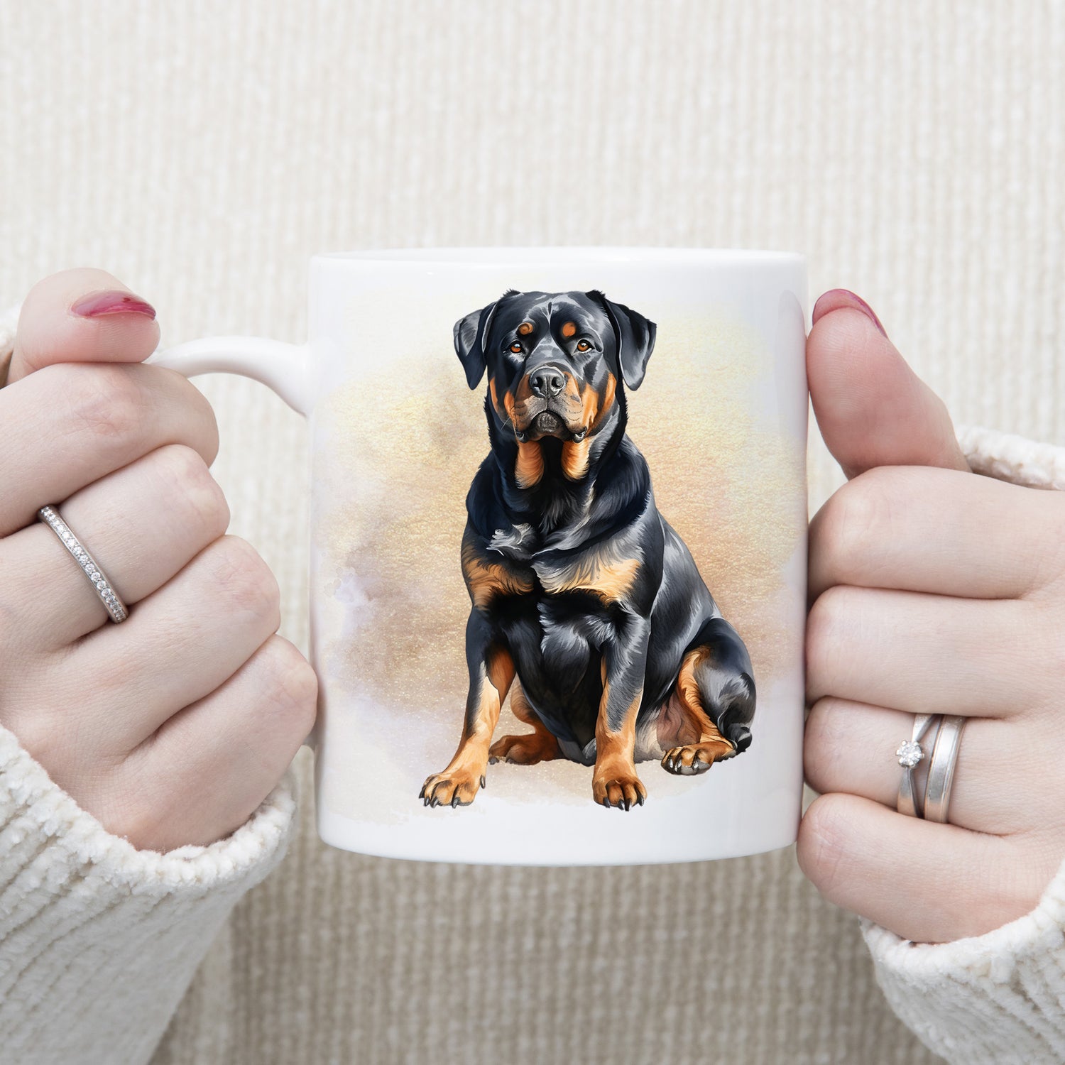 A woman is holding white ceramic mug showing a Rottweiler dog sitting in front of a brown and gold misty background.