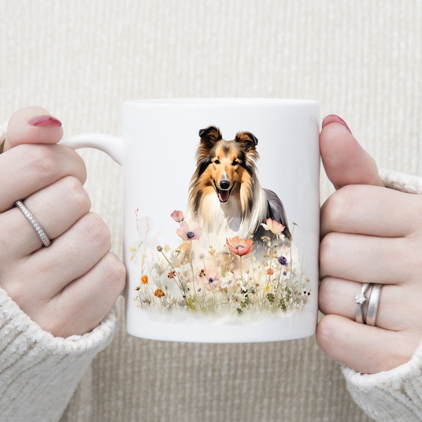 A white ceramic mug shows a tri-coloured Rough Collie standing among a range of wildflowers.  The mug is being held by a woman.
