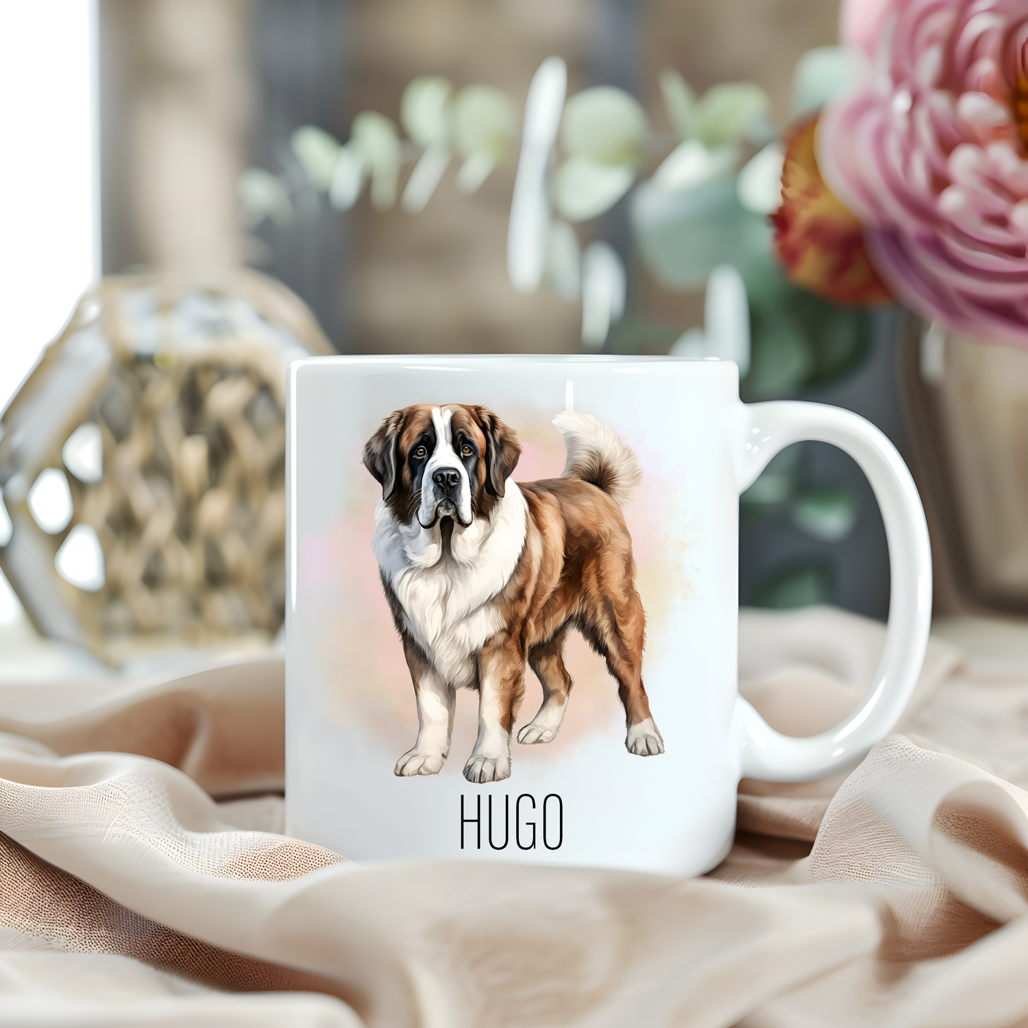 A happy Saint Bernard dog is stood within a misty background on a white personalised ceramic mug which has been placed on a beige cloth.  A large pink flower with green foliage accessorizes the image.