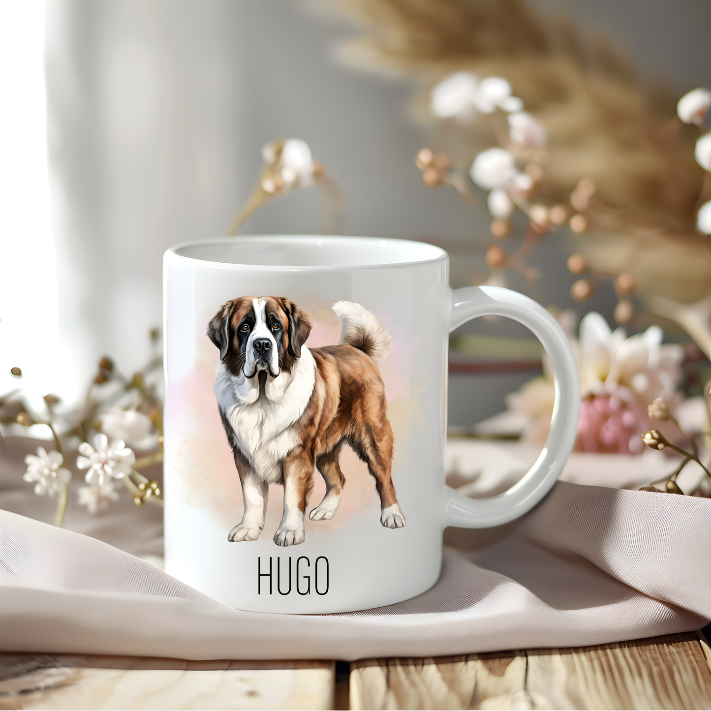 A lovely Saint Bernard coffee mug personalised with a pet name.  The mug sits on a wooden surface with a creamy coloured cloth and a variety of flowers decorate the background.