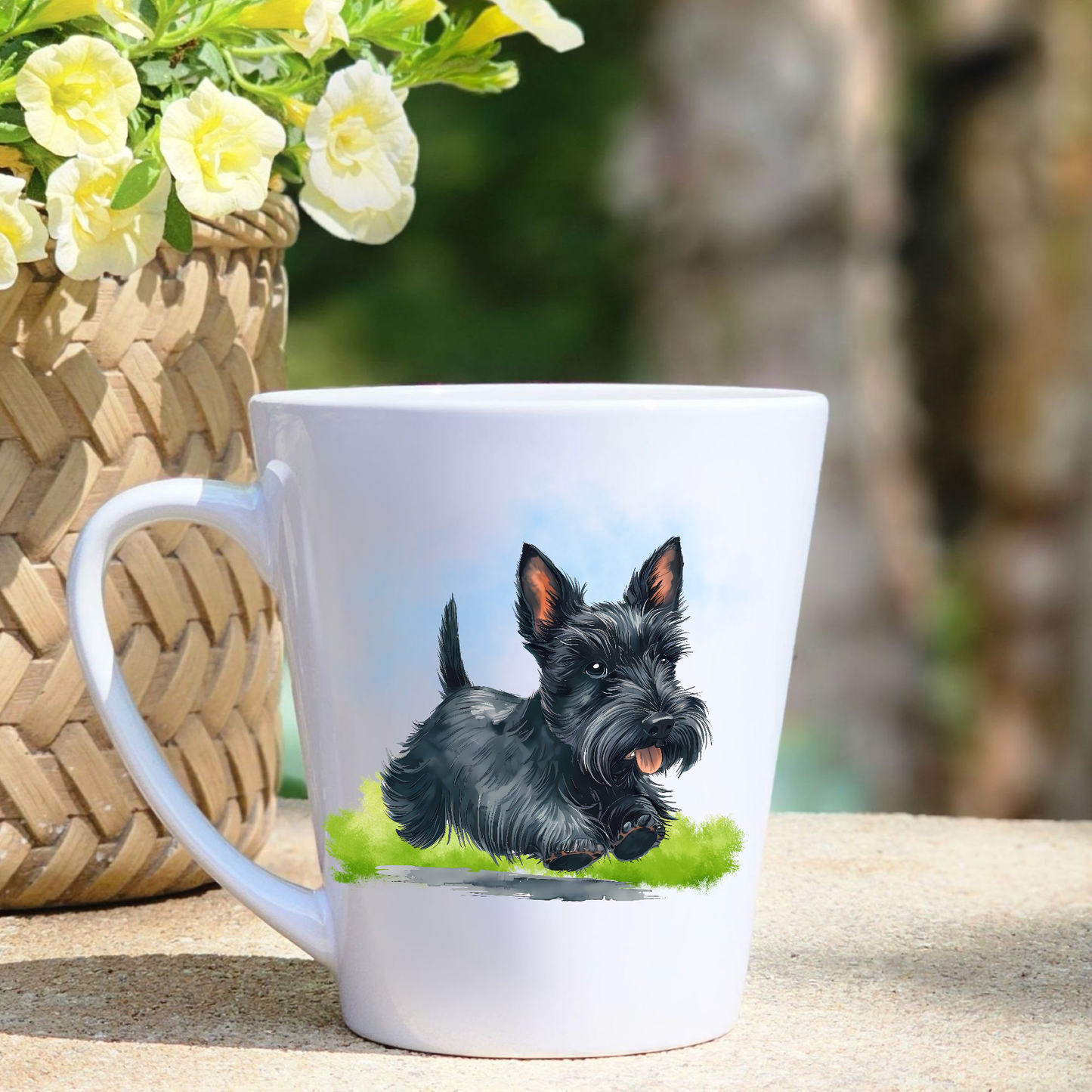 A white ceramic latte mug featuring a black Scottish Terrier running on a grassy surface.  A basket containing yellow flowers sits to the left-hand side. 