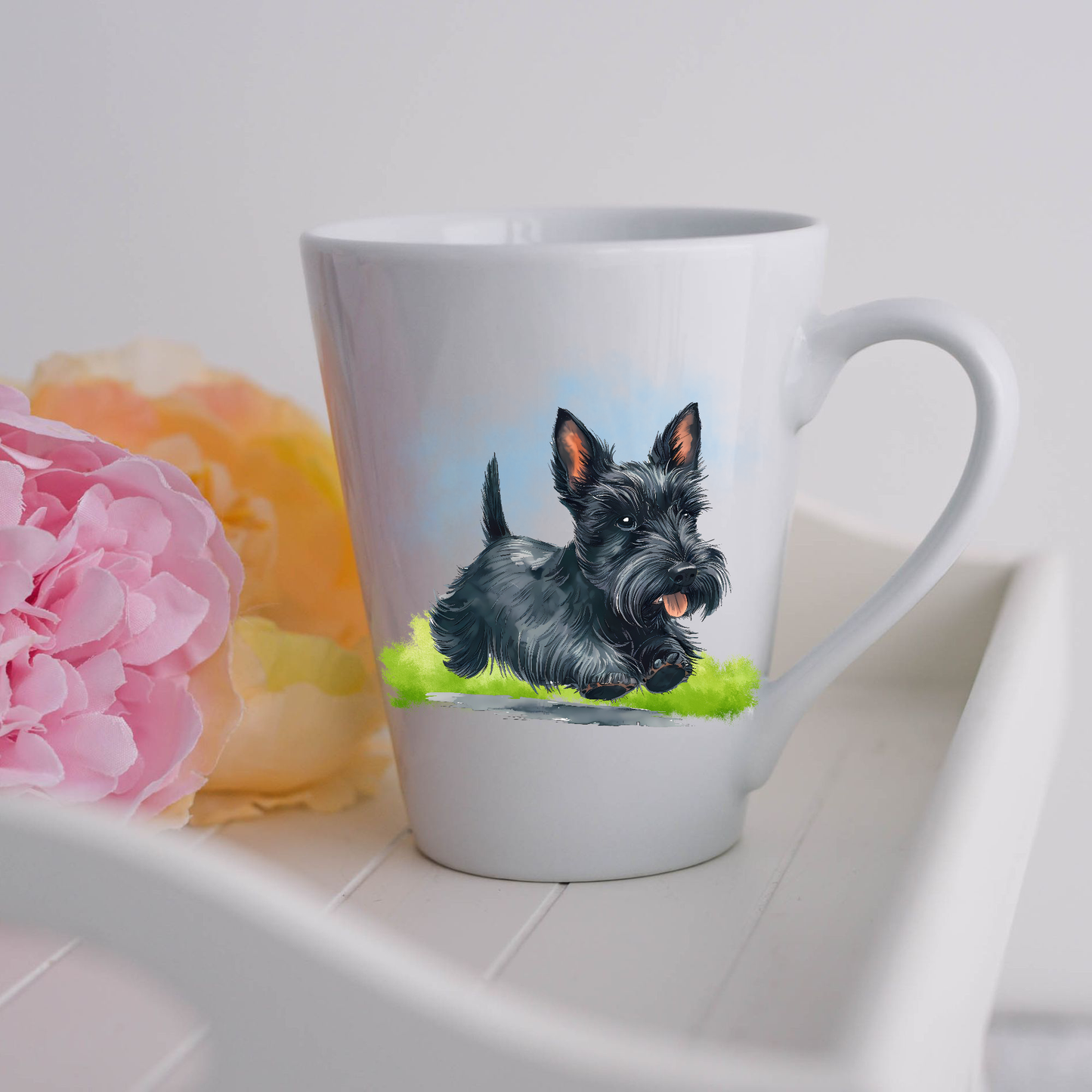 A black Scottish Terrier is seen on a white ceramic latte mug running on a grassy surface.  The mug is placed on a white tray with pink and yellow flowers. 