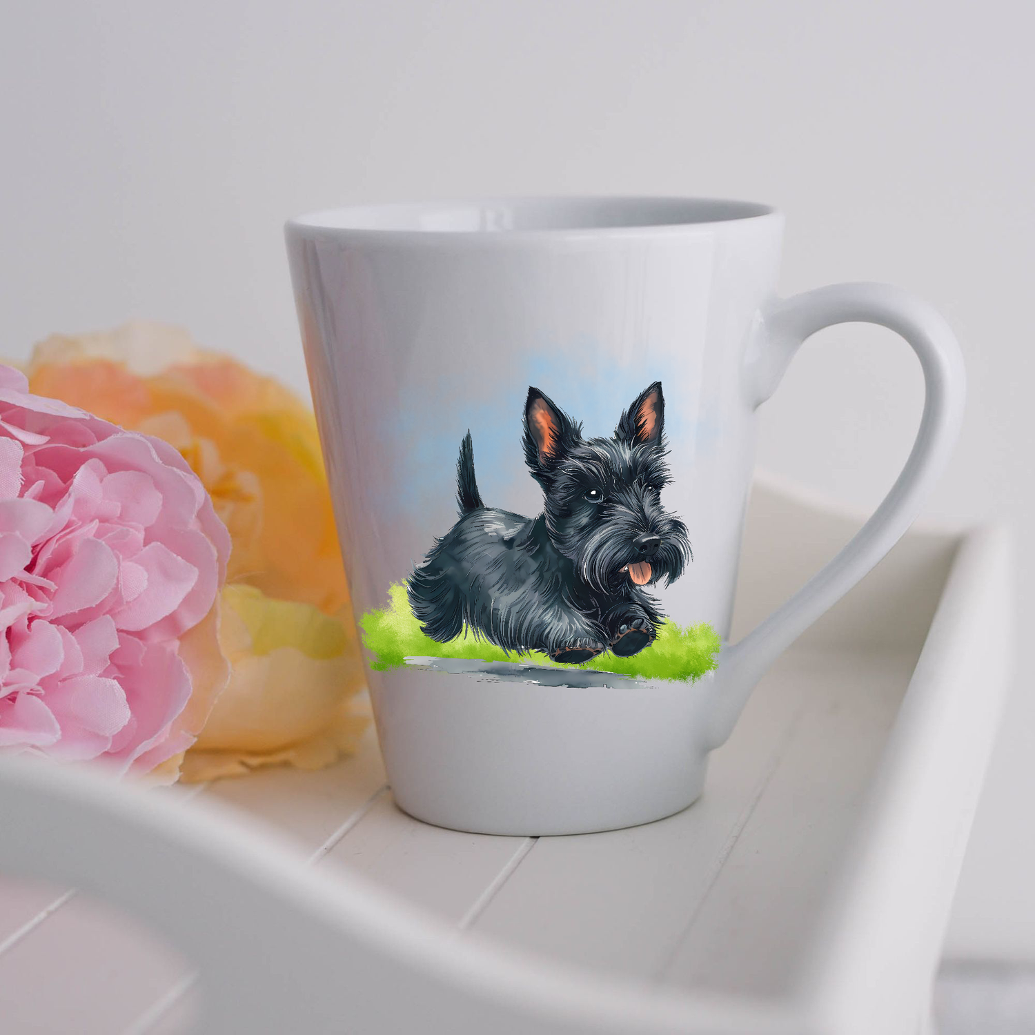 A black Scottish Terrier is seen on a white ceramic latte mug running on a grassy surface.  The mug is placed on a white tray with pink and yellow flowers. 