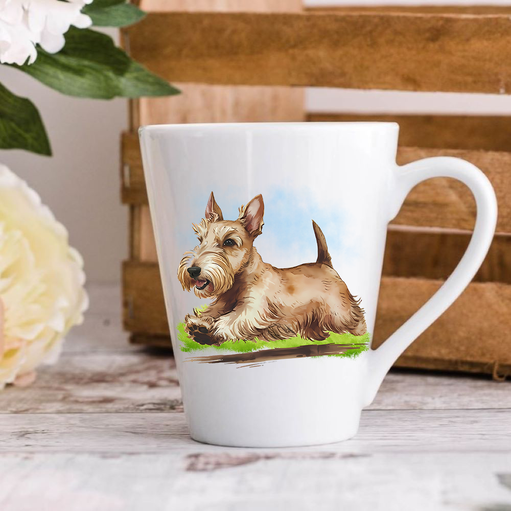 A white ceramic latte mug stands on a wooden surface with a crate in the background. The mug features a Wheaten Scottish Terrier running on a grassy surface.  A large yellow flower peeps in from the left-hand side.